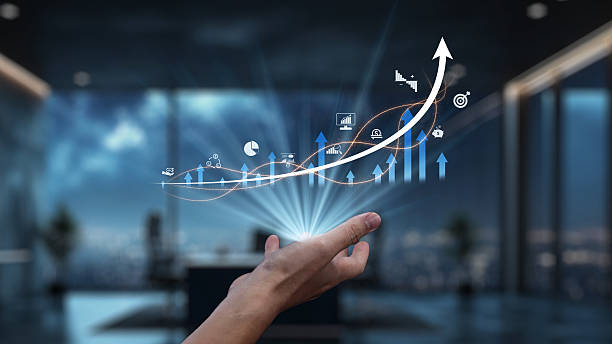 A close-up of a hand reaching out towards a digital growth graph featuring various charts and arrows in a sleek office setting.